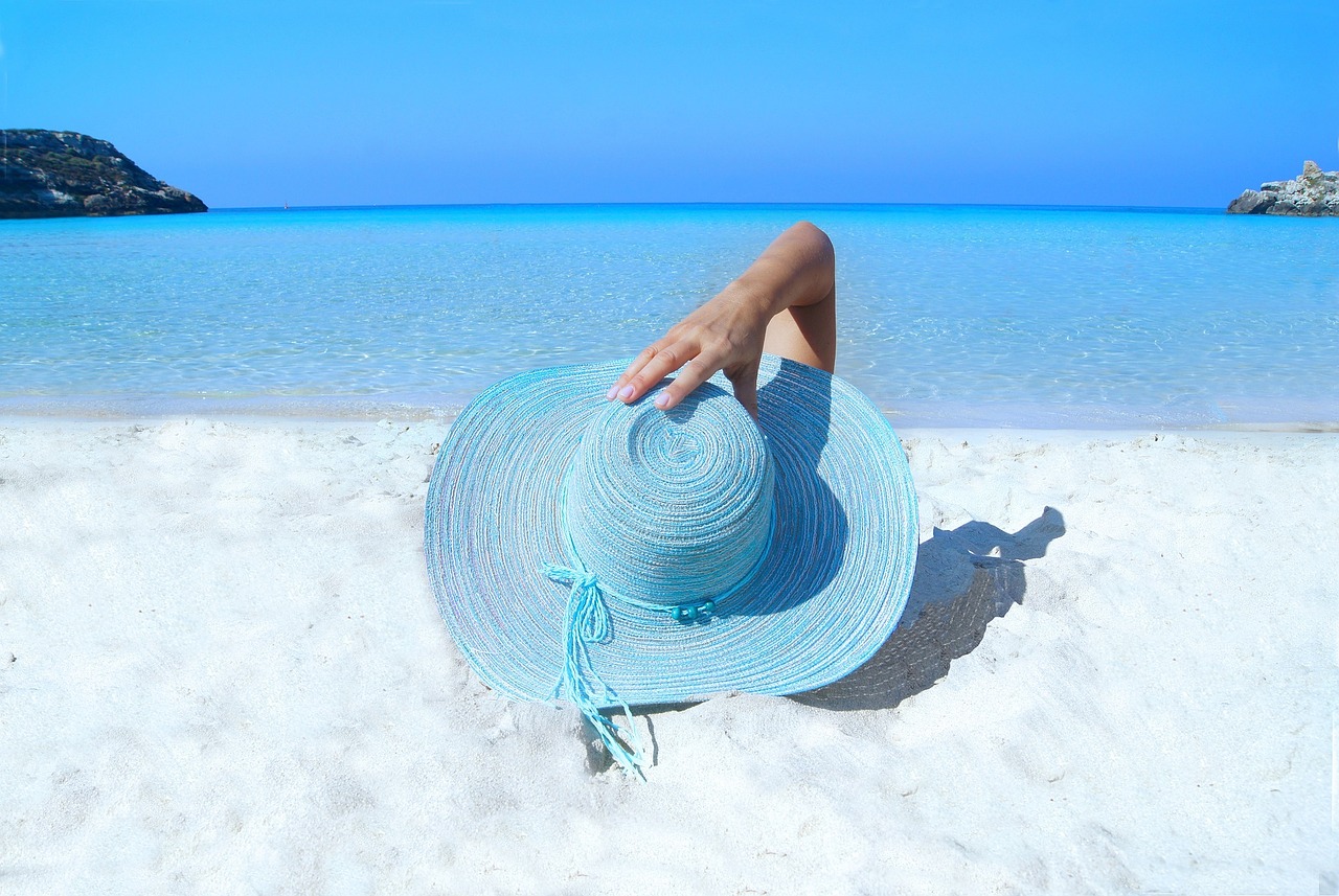 Eine Frau mit einem blauen Hut am Strand, Umgang mit Sonne.