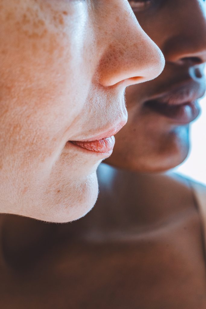 Nahaufnahme von zwei Personen, wobei der Fokus auf ihren Gesichtern im Profil liegt. Das Bild erfasst ihre Nasen, M&uuml;nder und Teile ihrer Wangen und zeigt unterschiedliche Hautt&ouml;ne. Der Hintergrund ist leicht unscharf.
